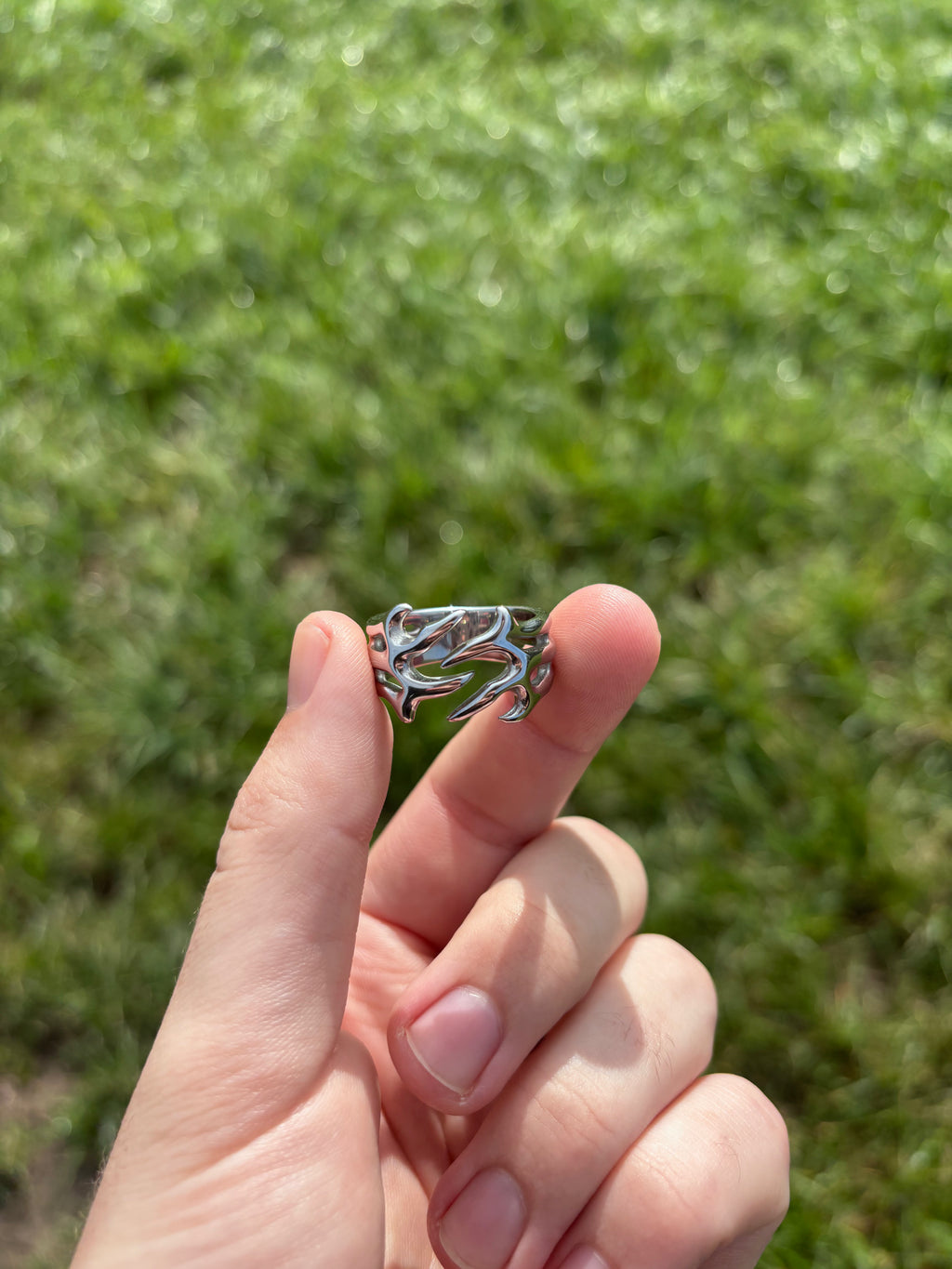 Thorn Embrace Ring aus 316L-Edelstahl zwischen zwei Fingern gehalten, durchbrochene Dornenform